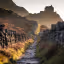 The image is well-composed, leading the eye along the pathway to the castle in the background. The lighting is warm and inviting, enhancing the scene. The image is generally sharp, although the depth of field is shallow, causing some blurring in the foreground. Colors appear accurate and realistic. The image is photo-realistic and the key elements, such as the pathway and the castle, are in focus. Overall, it's a high-quality landscape photograph.