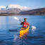 This image features a person kayaking on a lake with snow-capped mountains in the background. It's well-composed, with the kayaker providing a focal point. The lighting is good, highlighting the blue water and snow-capped mountains, and the image is reasonably sharp. The colors appear accurate and vibrant. The key elements, the kayaker and mountains, are in focus. The image is photo-realistic. Minor deductions might be given for some slight softness in the distant mountains.