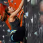 A woman actively engaged in indoor rock climbing, focusing on her upward movement and grip on the holds.