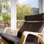 The image provides a clear view from an indoor space to an outdoor deck with a natural landscape. The lighting is natural and well-balanced, contributing to vibrant and accurate colors. The primary subjects, including the foreground chair and the deck, are in focus, though the distant background elements like the mountains appear softer.