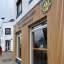 The image shows the exterior of the 'West Highland Tea Company'. The composition is decent, but the image isn't perfectly sharp. The lighting appears natural, possibly overcast, which results in even illumination but lacks strong highlights or shadows. Color accuracy seems reasonable. It's fairly photo-realistic. The key elements, such as the company name and the building's facade, are generally in focus. However, the overall image quality could be improved with better sharpness and more dynamic lighting.
